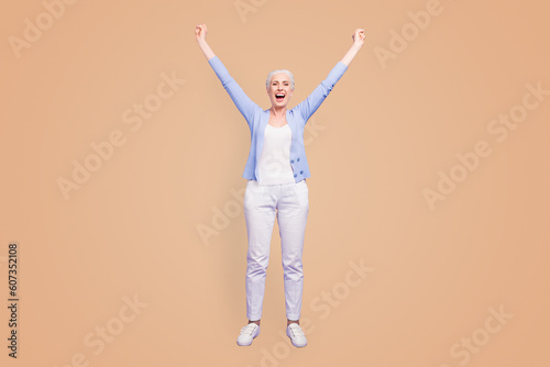 Full length size body vertical portrait of grey haired old confident woman wearing casual, shoes footwear, raising hands up, celebrating winning. Isolated over violet purple background