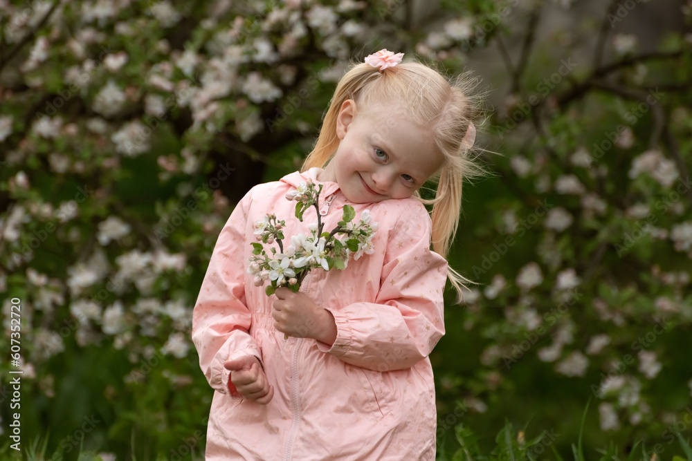 Blonde cuty girl in pink outfit with two tails holds flowering branch on blooming tree background. Blonde cuty girl in pink outfit with two tails holds flowering branch on blooming tree background.