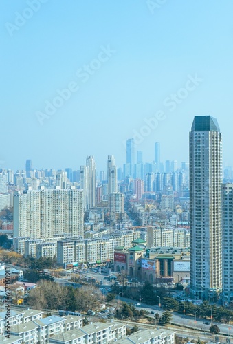 Vertical shot of cityscape with urban towers and skyscrapers over houses under blue sky © Hokutolite G/Wirestock Creators