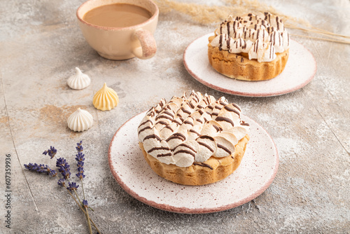 Two tartlets with meringue cream and cup of coffee on brown concrete, side view.