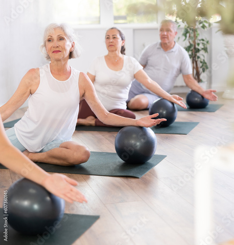 Group of elderly people doing pilates exercises with soft ball on mat in fitness studio
