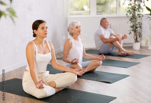 Women sitting on mats in Lotus Position Padmasana during yoga stretch joint workout in fitness center