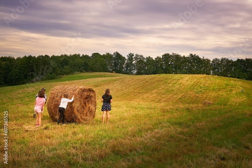 View of a group of young girls attempting to roll a round hay bale in a field