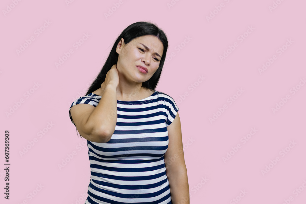 Young asian brunette woman is suffering from neckache. Isolated on pink background.