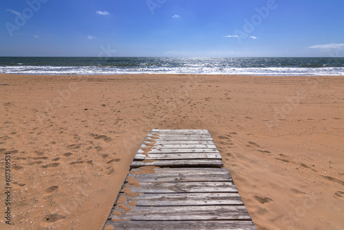 The beauty of a beach with a wooden boardwalk stretching along the sandy shoreline. The path guides visitors towards the stunning ocean  creating a peaceful and scenic atmosphere. 