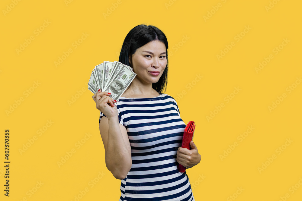 Asian woman is showing fan of dollar banknotes. Standing over yellow background. Asian woman is showing fan of dollar banknotes. Standing over yellow background.