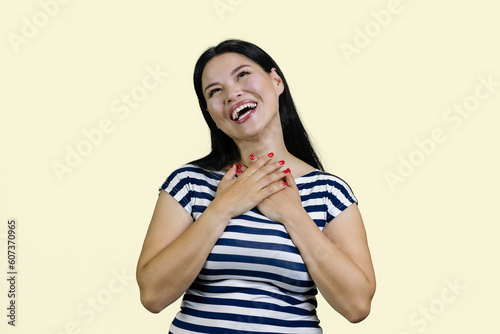 Young asian is lauging loudly white touching her chest. Isolated on pastel yellow background. photo