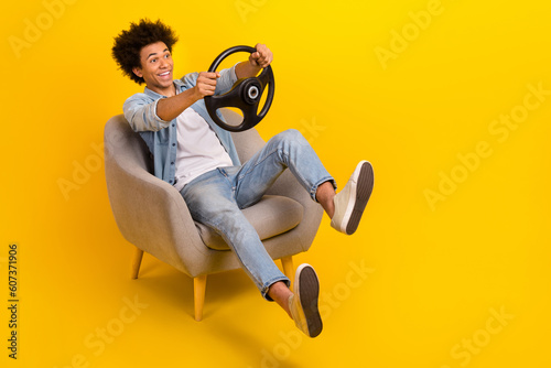Full size photo of overjoyed carefree person sit chair hands hold wheel empty space isolated on yellow color background photo