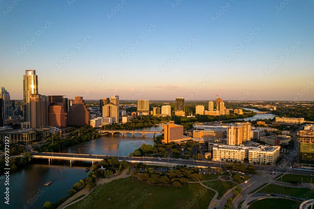 Drone shot of TX skyline with waterfront, greenery and blue sky at sunset in Austin city