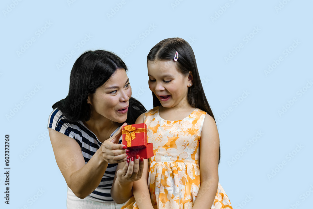 Young brunette lady is giving an opened gift box to her happy little princess. Isolated on pale blue background. Young brunette lady is giving an opened gift box to her happy little princess. Isolated on pale blue background.
