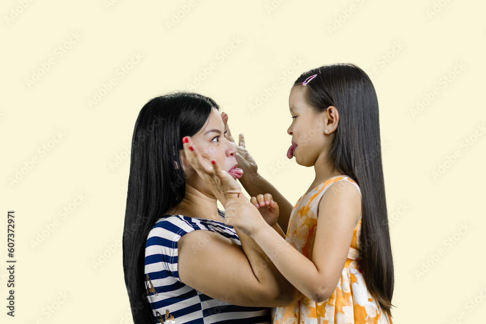Side view of woman and little girl are making faces to each other. Isolated on pastel yellow background. Side view of woman and little girl are making faces to each other. Isolated on pastel yellow background.
