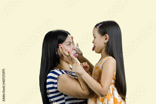 Side view of woman and little girl are making faces to each other. Isolated on pastel yellow background.