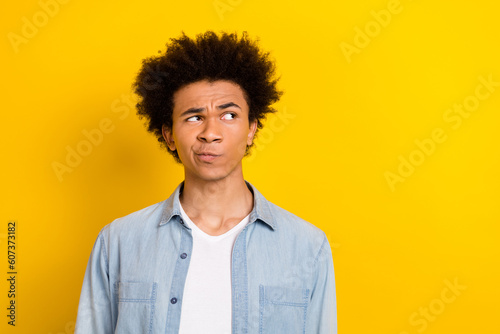 Photo of doubtful unsure guy dressed denim shirt looking empty space isolated yellow color background