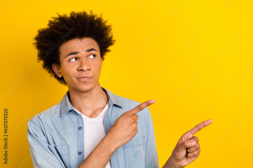 Photo of funky suspicious guy dressed denim shirt looking showing two fingers empty space isolated yellow color background Photo of funky suspicious guy dressed denim shirt looking showing two fingers empty space isolated yellow color background