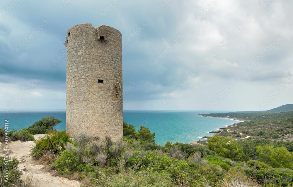 Round stone tower on the shore of Mediterranean Sea on blue cloudy sky background in Spain