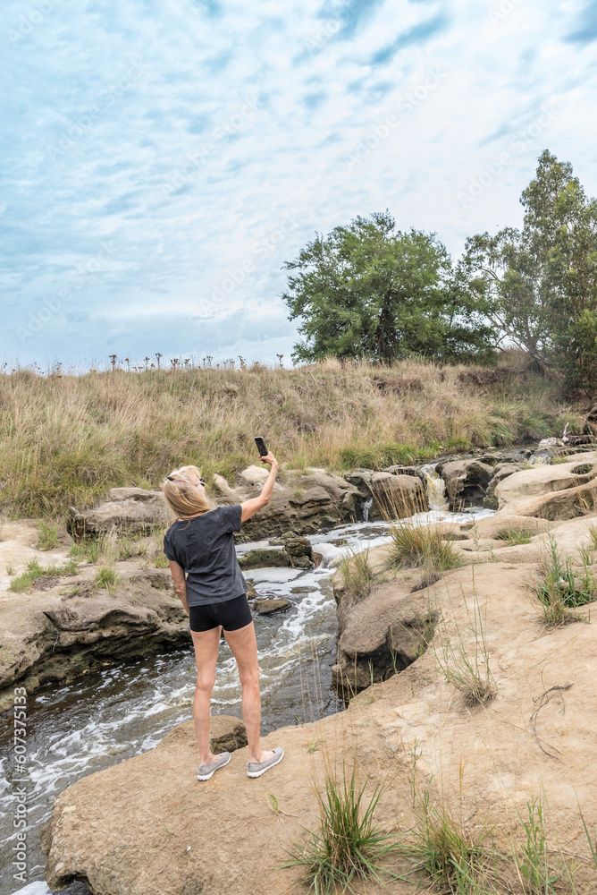 Fototapeta premium Adventurer woman taking selfies with mobile phone outdoors near a water stream.