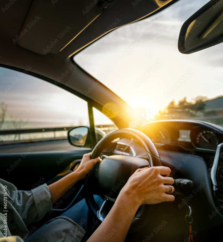 Female hands on the steering wheel of a car. Woman driving a car at sunset on the seashore. Auto travel concept