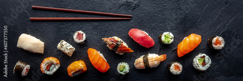 Sushi overhead flat lay panorama with chopsticks. Rolls, maki, nigiri on a black slate background, Japanese food. Salmon, eel, shrimp, tuna etc with rice