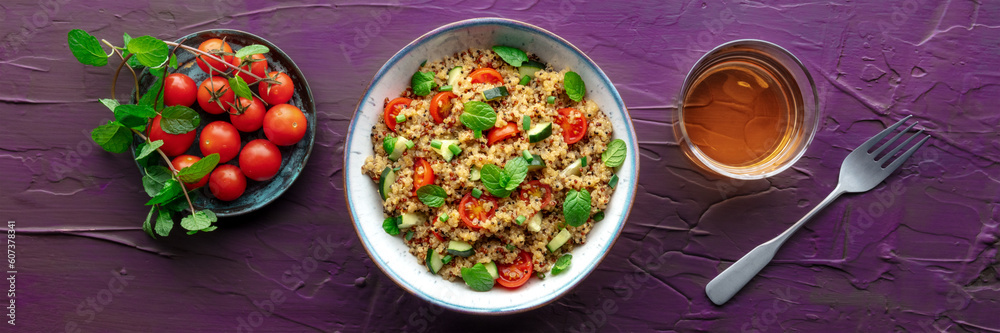 Quinoa tabbouleh salad in a bowl panorama, a healthy dinner with tomatoes and mint, overhead flat lay shot with a drink on a purple background