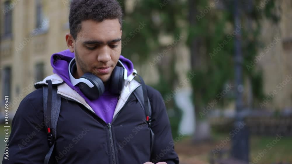 Troubled thoughtful African American young man with smartphone standing at university campus looking around talking. Stressed anxious student waiting for exam result outdoors Troubled thoughtful African American young man with smartphone standing at university campus looking around talking. Stressed anxious student waiting for exam result outdoors
