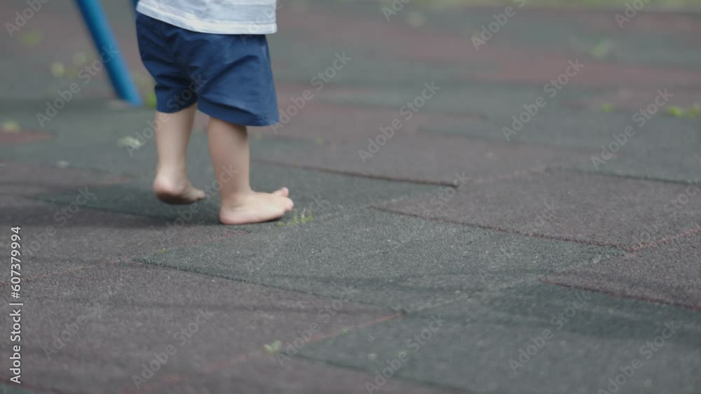 small child bare feet walking on playground summer day outdoors. bare legs baby kid blue shorts on dirty coating. Concept of hardening children, health, development of feeling, nature, orthopedic small child bare feet walking on playground summer day outdoors. bare legs baby kid blue shorts on dirty coating. Concept of hardening children, health, development of feeling, nature, orthopedic