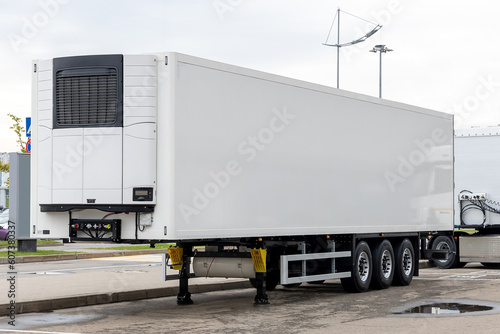 A new white refrigerated semi-trailer in the parking lot, waiting to be loaded with cargo. Freight commercial transport