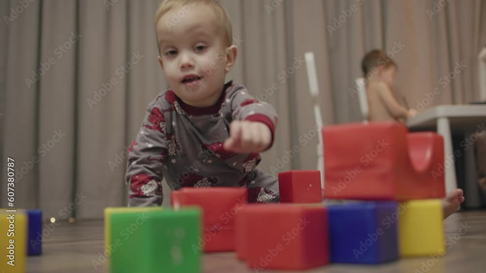 kid toddler sits floor gray pajamas plays multi-colored plastic cubes builds tower destroys with feet and hands, child learns break and build. problem upbringing, disobedience, crisis children concept kid toddler sits floor gray pajamas plays multi-colored plastic cubes builds tower destroys with feet and hands, child learns break and build. problem upbringing, disobedience, crisis children concept
