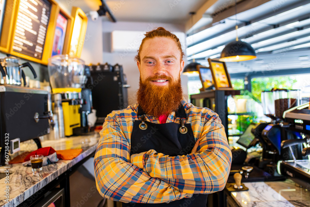 Professional barista young redhaired ginger bearded man in black apron working in coffee shop