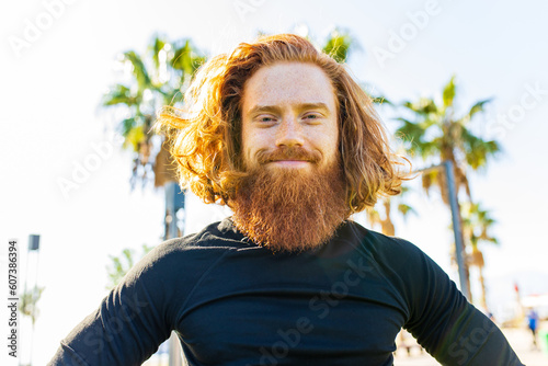handsome redhaireb man with long beard wear black sporty suit and warming up in sunny beach photo