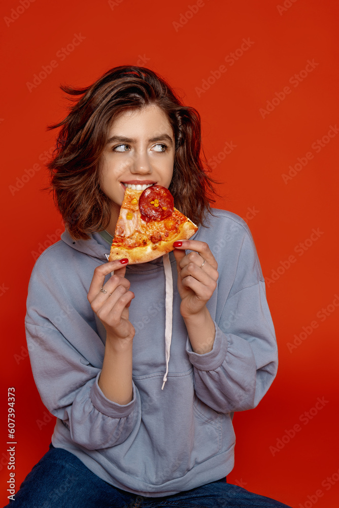 a young girl on an orange background in casual clothes bites a pizza a young girl on an orange background in casual clothes bites a pizza