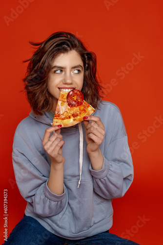 a young girl on an orange background in casual clothes bites a pizza