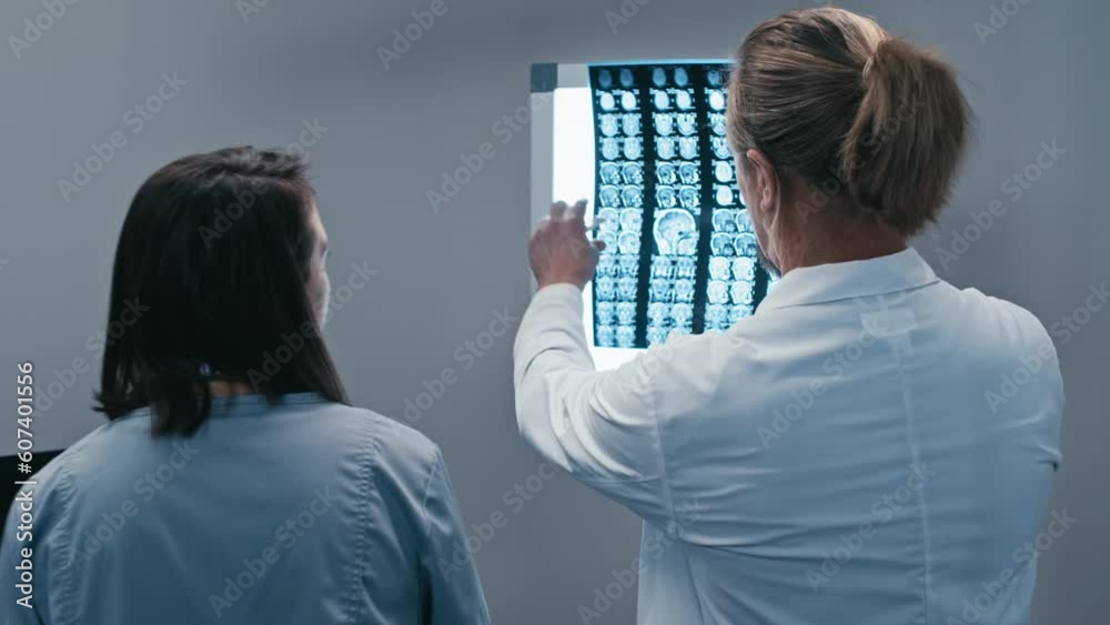 Rear view shot of two modern doctors working together in hospital placing brain X-ray scan image onto lightbox Rear view shot of two modern doctors working together in hospital placing brain X-ray scan image onto lightbox