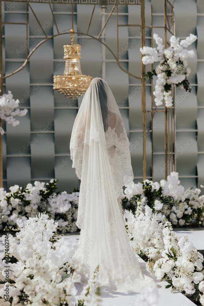A bride in a white wedding dress stands in front of a luxury elegant wedding decoration.