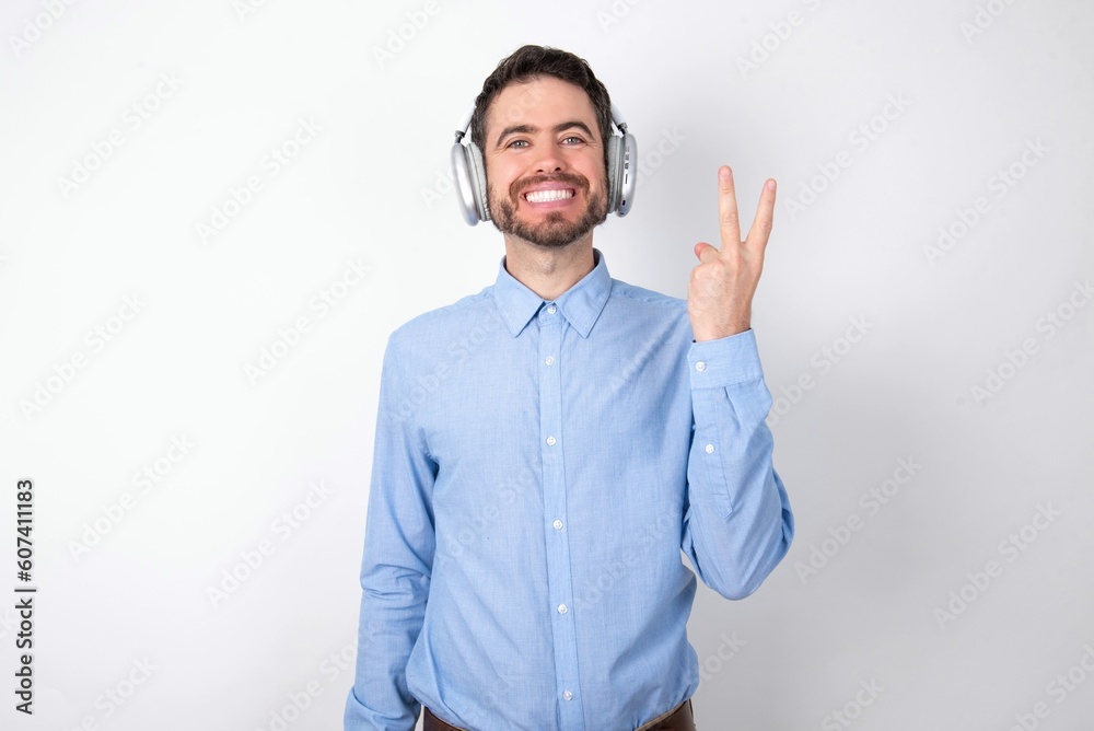 businessman wearing blue t-shirt with headphones over white background smiling and looking friendly, showing number two or second with hand forward, counting down businessman wearing blue t-shirt with headphones over white background smiling and looking friendly, showing number two or second with hand forward, counting down