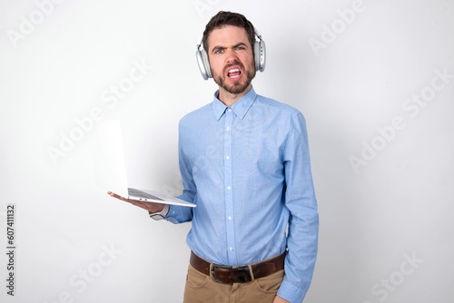 Obraz na płótnie Portrait of dissatisfied businessman wearing blue t-shirt with headphones over w