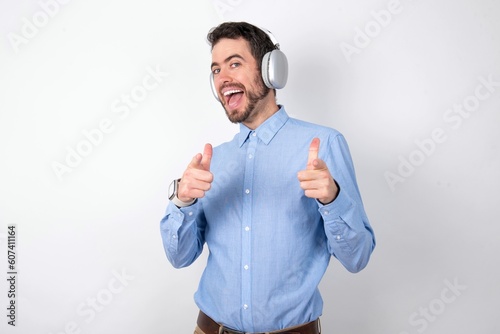 businessman wearing blue t-shirt with headphones over white background directs fingers at camera selects someone. I recommend you. Best choice