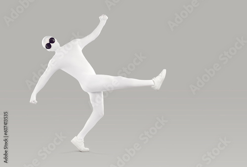 Full length portrait of a funny, happy man in a white, faceless, skintight, spandex bodysuit costume disguise and black, round sunglasses walking or dancing isolated on a grey color background