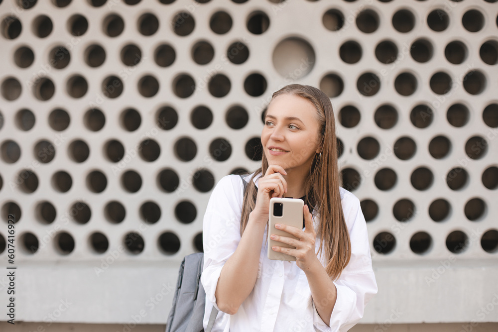 Thinking dreaming young beautiful woman posing near wall with circle in city background using mobile phone. Thinking dreaming young beautiful woman posing near wall with circle in city background using mobile phone.