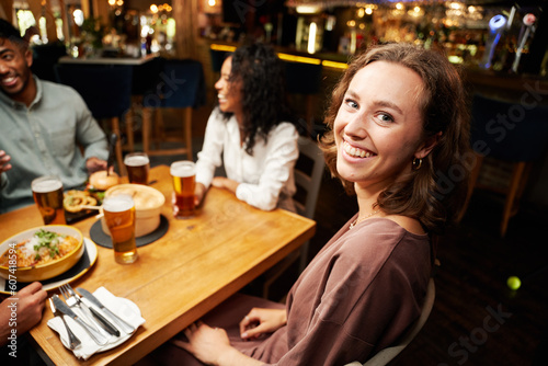 Happy young multiracial group of friends in casual clothing sitting around table at bar