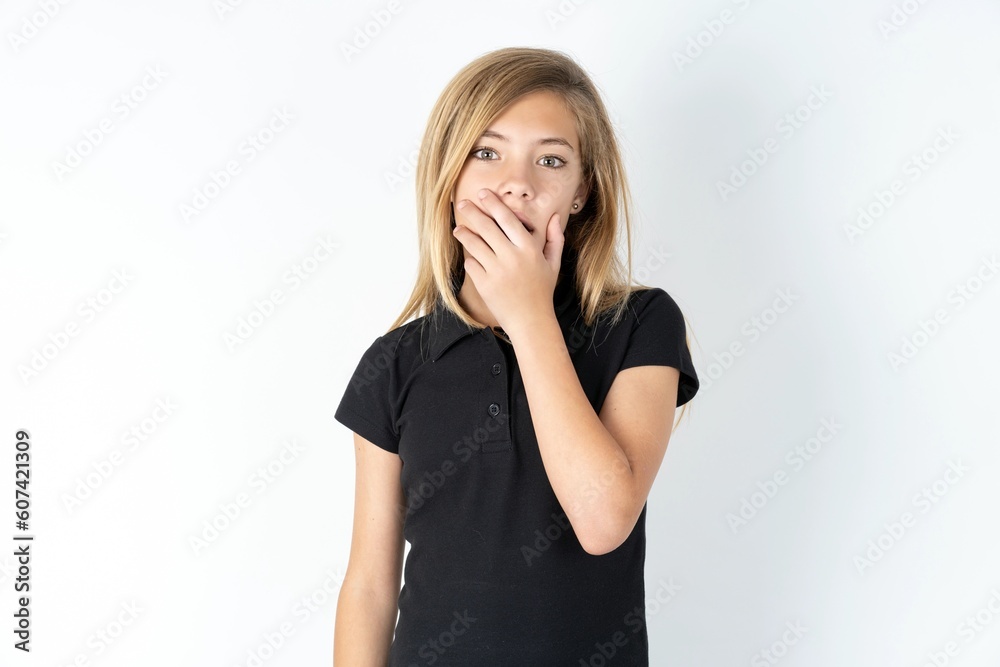 Emotional beautiful teen girl wearing black dress over white studio background gasps from astonishment, covers opened mouth with palm, looks shocked at camera. Emotional beautiful teen girl wearing black dress over white studio background gasps from astonishment, covers opened mouth with palm, looks shocked at camera.