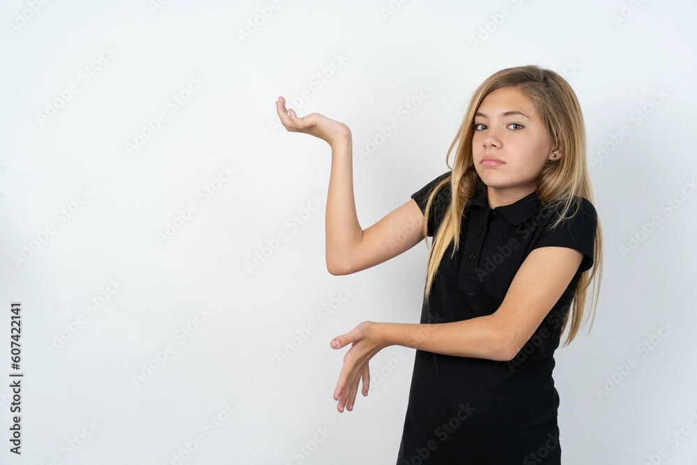 beautiful teen girl wearing black dress over white studio background pointing aside with both hands showing something strange and saying: I don't know what is this. Advertisement concept. beautiful teen girl wearing black dress over white studio background pointing aside with both hands showing something strange and saying: I don't know what is this. Advertisement concept.