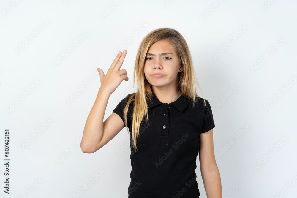 Unhappy beautiful teen girl wearing black dress over white studio background makes suicide gesture and imitates gun with hand, curves lips, keeps two fingers on temple Unhappy beautiful teen girl wearing black dress over white studio background makes suicide gesture and imitates gun with hand, curves lips, keeps two fingers on temple