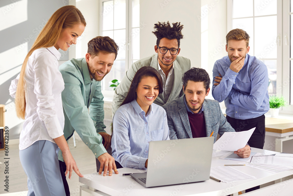 Smiling team of employees looking at laptop screen together. Diverse cheerful young colleagues watching webinar, making conference video call, working with computer at meeting Smiling team of employees looking at laptop screen together. Diverse cheerful young colleagues watching webinar, making conference video call, working with computer at meeting