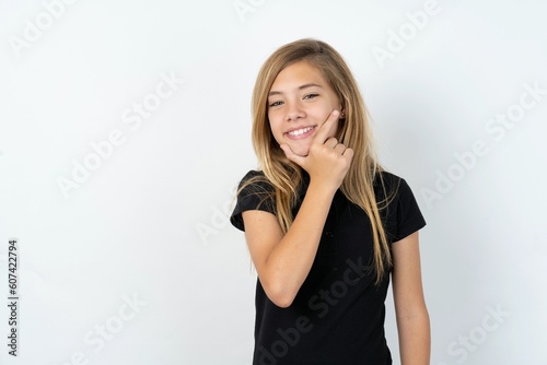 beautiful teen girl wearing black dress over white studio background looking confident at the camera smiling with crossed arms and hand raised on chin. Thinking positive.