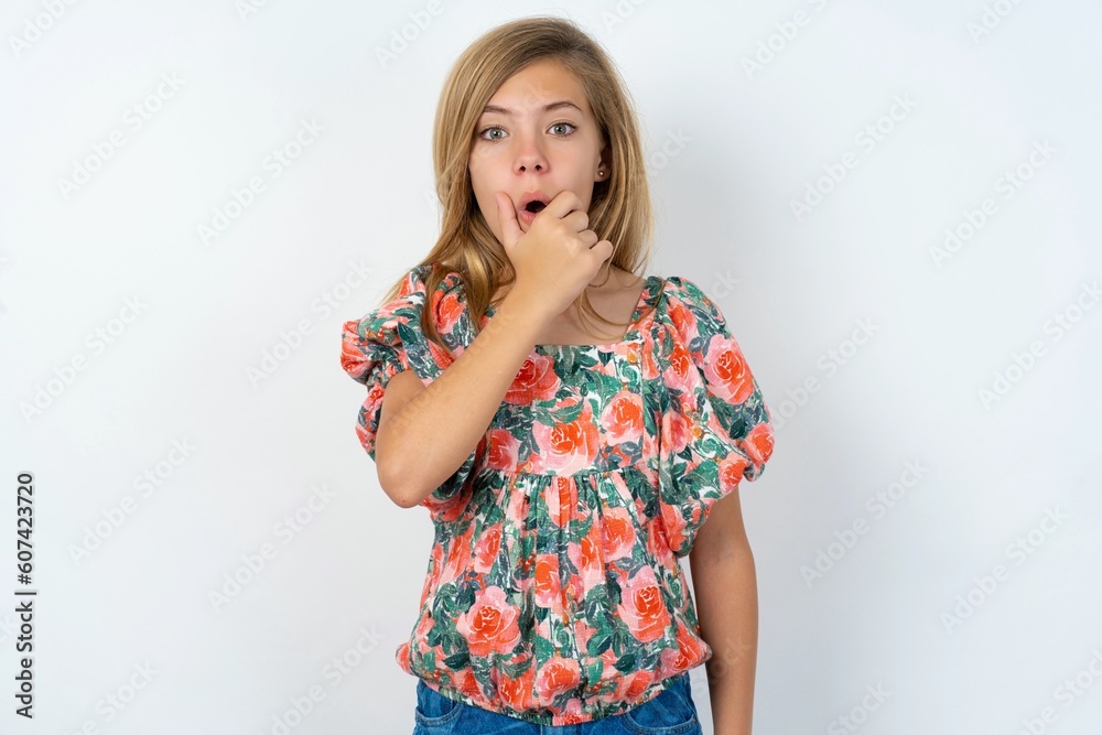 beautiful teen girl wearing flowered dress over white studio background Looking fascinated with disbelief, surprise and amazed expression with hands on chin beautiful teen girl wearing flowered dress over white studio background Looking fascinated with disbelief, surprise and amazed expression with hands on chin