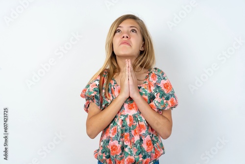 beautiful teen girl wearing flowered dress over white studio background begging and praying with hands together with hope expression on face very emotional and worried. Please God