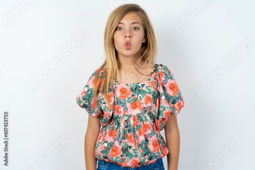 beautiful teen girl wearing flowered dress over white studio background making fish face with lips, crazy and comical gesture. Funny expression.