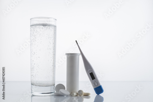 Pack of pills and capsules glass of water and a thermometer on a white background with space for text