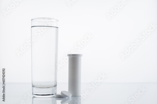 Glass of water and various packages of pills and capsules on the table on a white background with space for text