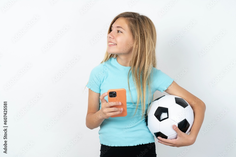 beautiful caucasian teen girl wearing sportswear holding a football ball over white wall holding in hands showing new cell beautiful caucasian teen girl wearing sportswear holding a football ball over white wall holding in hands showing new cell